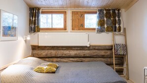 A cozy cabin room with a bed, two windows, a radiator, and a ladder.