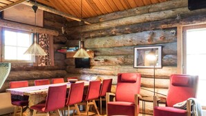 A log cabin interior with a wooden dining table, red chairs, a wooden floor, a hanging pendant light, and a framed picture on the wall.