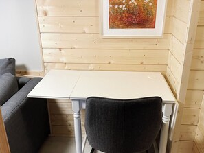 A small room with a white table and a black chair, wooden walls, and a framed picture on the wall.