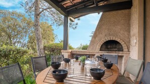 An outdoor dining area with a brick oven, wooden table, and chairs.