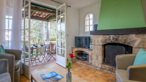 A living room with a stone fireplace, a TV, and a dining area with outdoor seating.