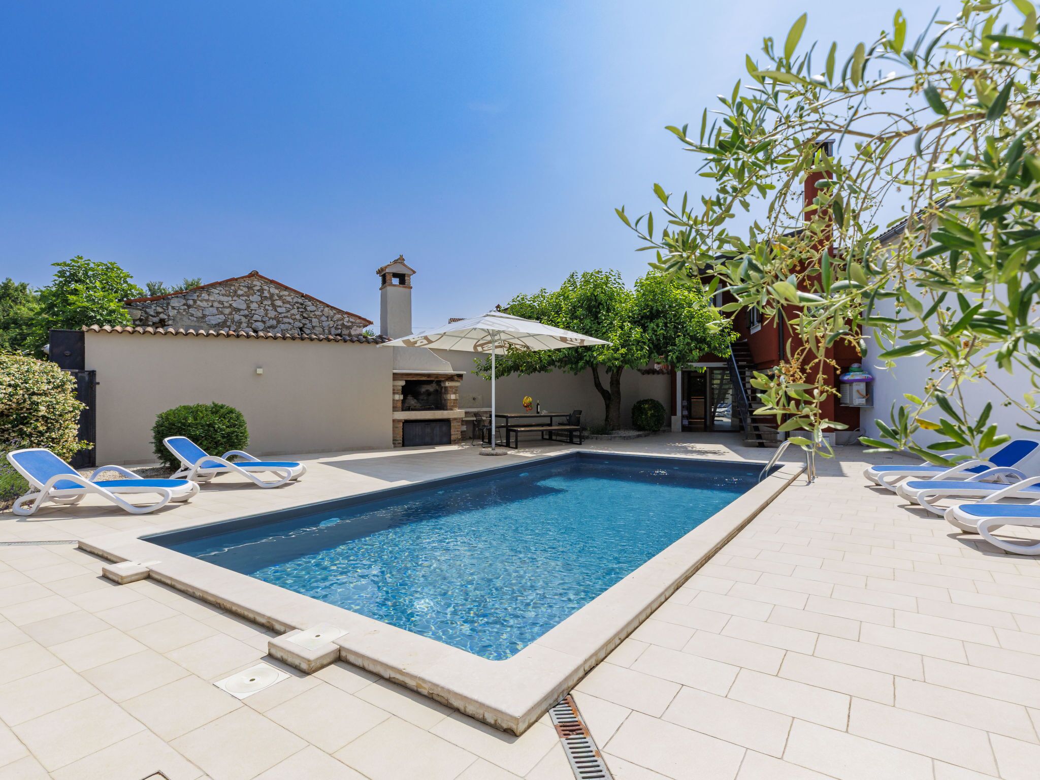 Une piscine rectangulaire avec des chaises longues et un espace barbecue.