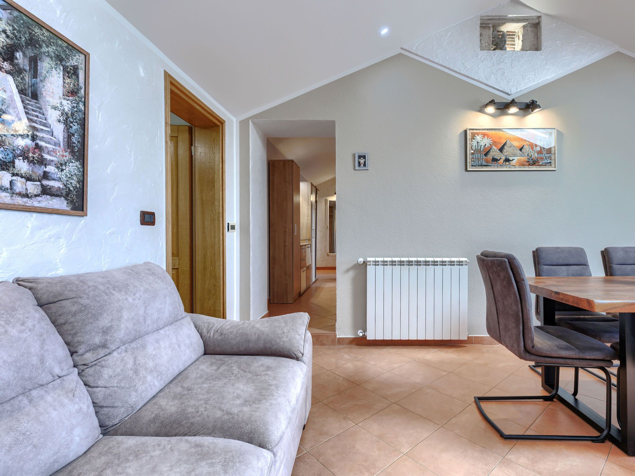 Ein modernes Wohnzimmer mit einer grauen Couch, einem Esstisch mit Stühlen, einer Heizung und Bildern an den Wänden.