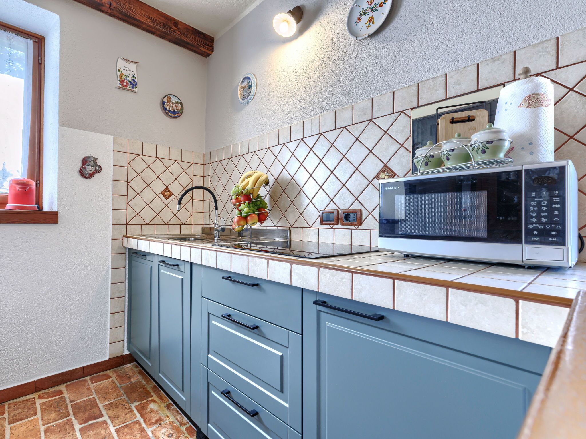 A kitchen with a tiled backsplash, a microwave, a fruit basket, and a sink.