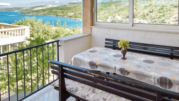 Un balcon doté d’une table et d’un banc, offrant une vue panoramique sur une zone côtière avec un plan d’eau et de la végétation.