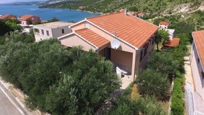 Une propriété située sur la côte, avec un toit recouvert de tuiles rouges, entourée de verdure et offrant une vue sur la mer.