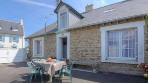 A stone house with a small porch, a table with chairs, and a garden with flowers. - Saint Ideuc by Interhome (Saint Malo)