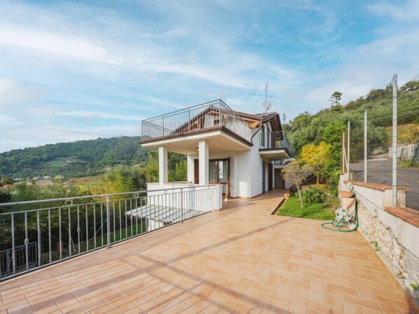 A two-story house with a balcony, a paved patio, and a view of a hilly landscape. - I Modellini by Interhome (Pietrasanta)