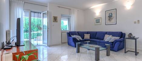 Ein modernes Wohnzimmer mit einem blauen Sofa, einem Glastisch und Blick auf Grünflächen.
