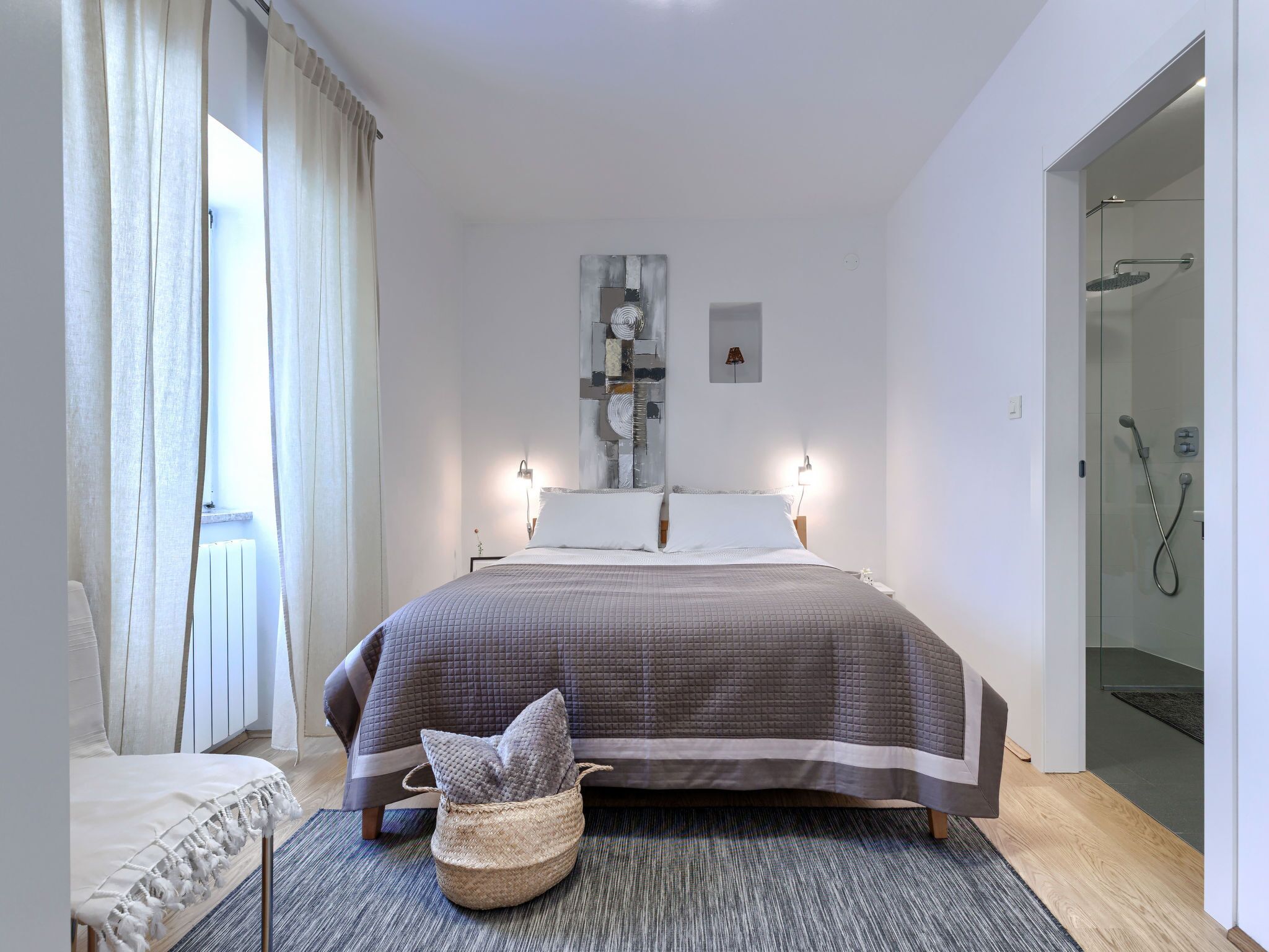 Une chambre moderne avec un grand lit, une table de chevet, une œuvre d’art accrochée au mur et une cabine de douche en verre.