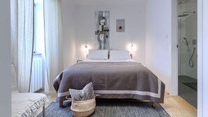 Une chambre moderne avec un grand lit, une table de chevet, une œuvre d’art accrochée au mur et une cabine de douche en verre.