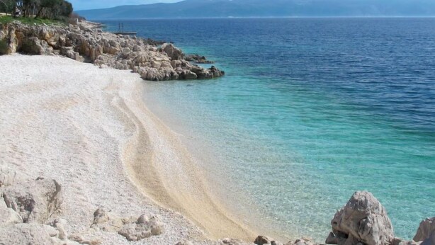 Une plage à l’eau turquoise et limpide, bordée d’un paysage rocheux.