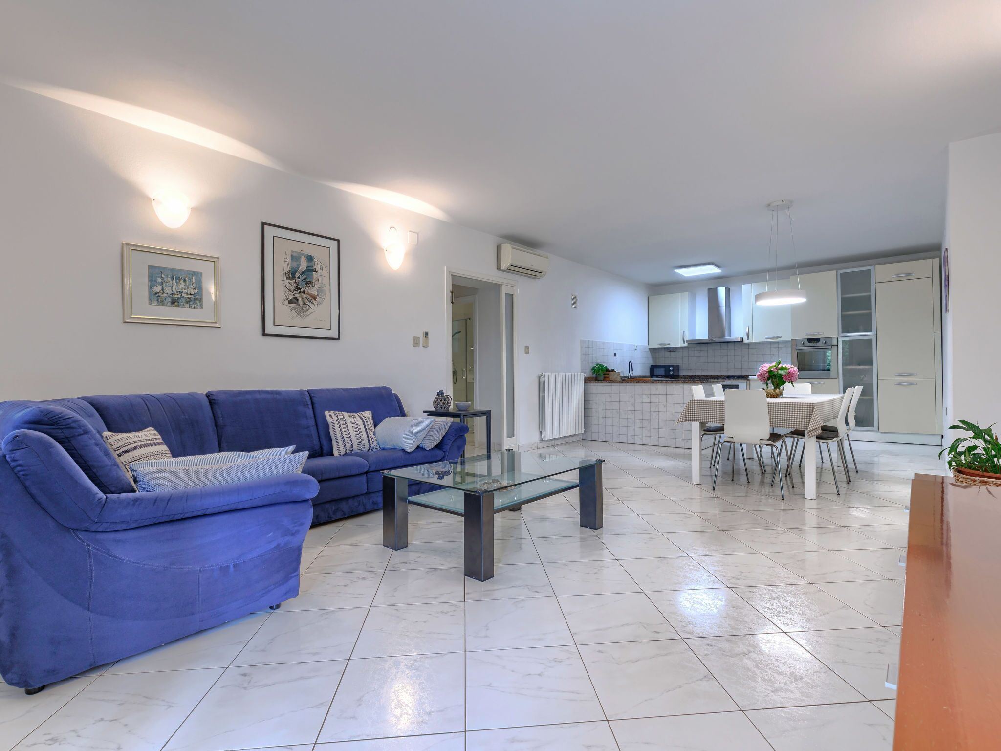 Un salon moderne avec un canapé bleu, une table basse en verre et un coin repas comprenant une table et des chaises blanches.