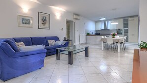 Un salon moderne avec un canapé bleu, une table basse en verre et un coin repas comprenant une table et des chaises blanches.