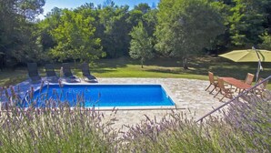 Une piscine rectangulaire bordée de pierres, entourée d’une terrasse aménagée avec des meubles d’extérieur et une table.