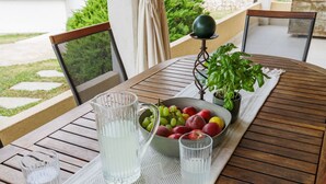 Une table en bois sur laquelle se trouvent une carafe d’eau, un saladier rempli de fruits et une plante en pot.