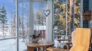 A cozy wooden deck with a round table and benches, large windows offering a view of a snowy forest. - Vacation home Ojala by Interhome (Kuusamo)