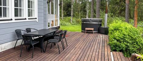 A wooden deck with a table and chairs, a hot tub, and a house with white trim and windows.