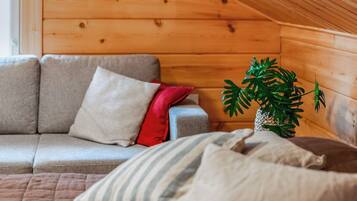 A cozy room with a wooden sloped ceiling, a sofa with cushions, and a potted plant.