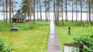 A wooden pathway leading to a small cabin by a lake, surrounded by tall trees. - Vacation home Ojala by Interhome (Kuusamo)