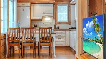 A cozy cabin interior with a dining area, kitchen, and a TV displaying a tropical beach scene.
