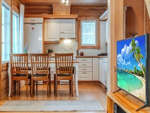 Interior acogedor de una cabaña con comedor, cocina y televisor mostrando una playa tropical.