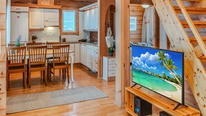 A cozy cabin interior with a dining area, kitchen, and a TV displaying a beach scene. - Vacation home Ojala by Interhome (Kuusamo)