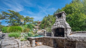Un área de barbacoa de piedra al aire libre con horno de piedra, rodeada por un muro de piedra y vegetación.