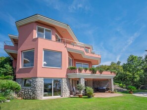 Uma casa moderna de dois andares com fachada rosa, janelas grandes e base de pedra.