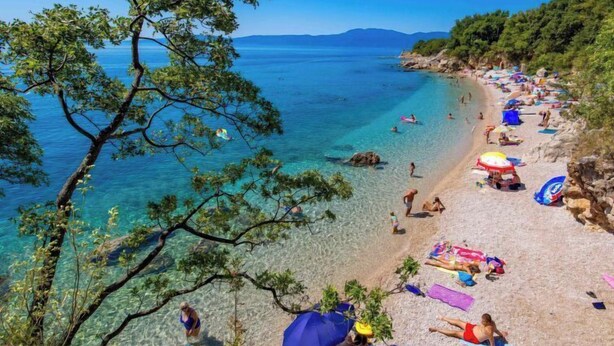 Una playa con agua cristalina, gente tomando el sol y sombrillas.
