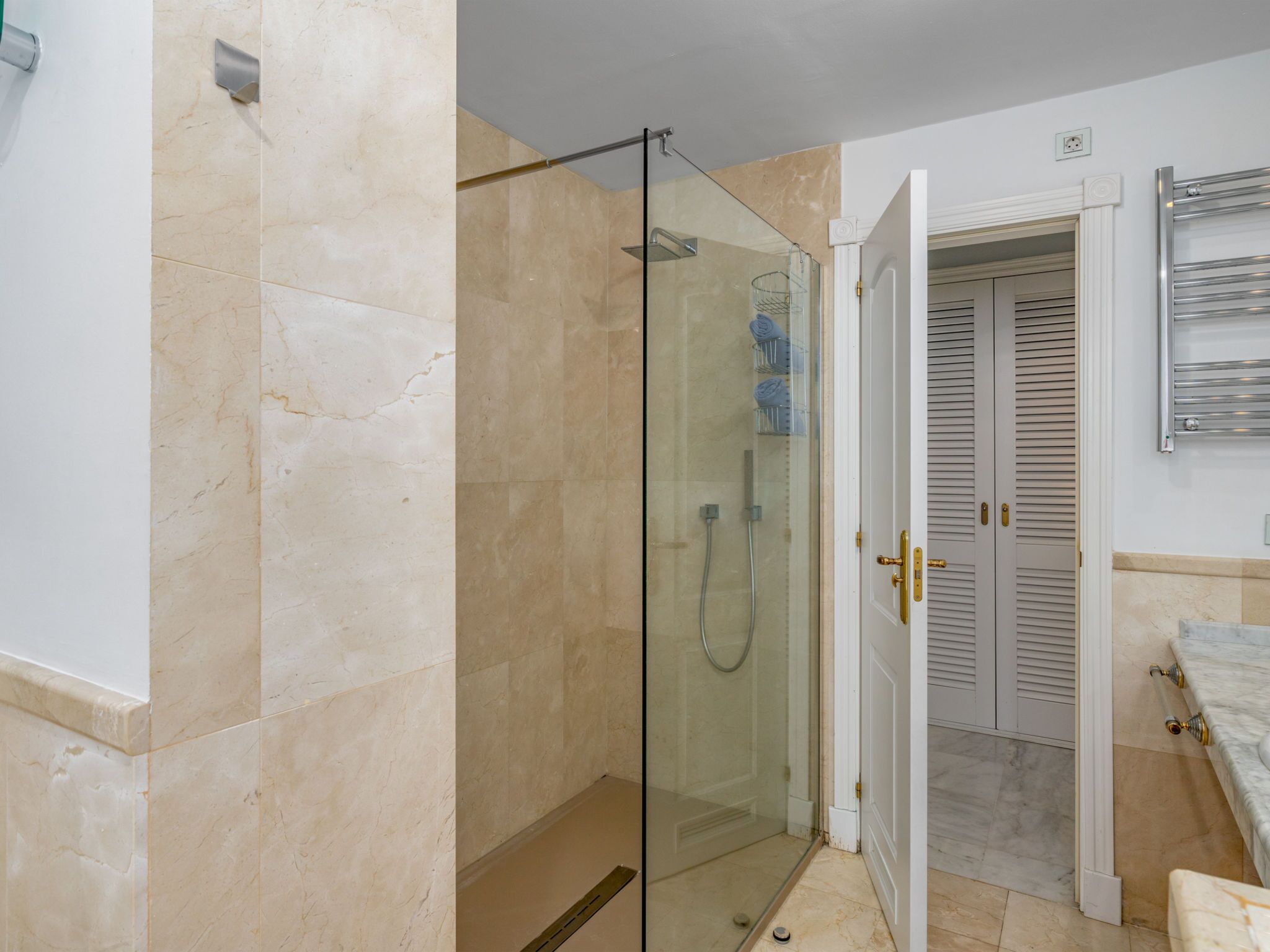 Ein Badezimmer mit einer Glaskabine zur Dusche, einer weißen Tür mit goldener Griff und einem Boden aus Marmorfliesen.