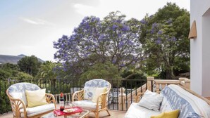 Een terras met rieten meubilair, een glazen tafel en uitzicht op paarse bloemen en bomen.