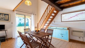 Un espace repas avec une table et des chaises en bois, un escalier et une vue sur l’extérieur.