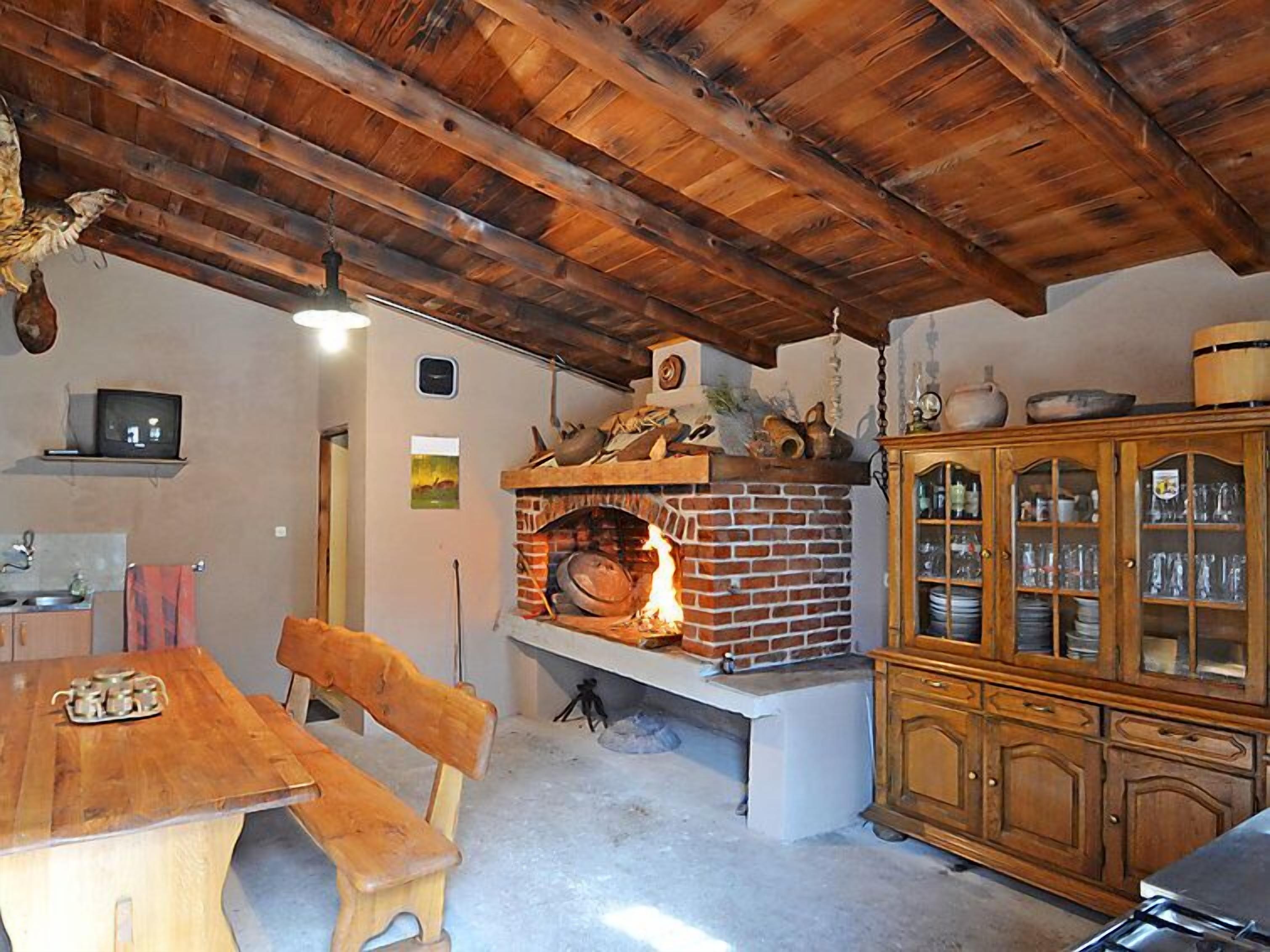 A rustic kitchen with a brick oven, wooden furniture, and a cabinet with glass doors.