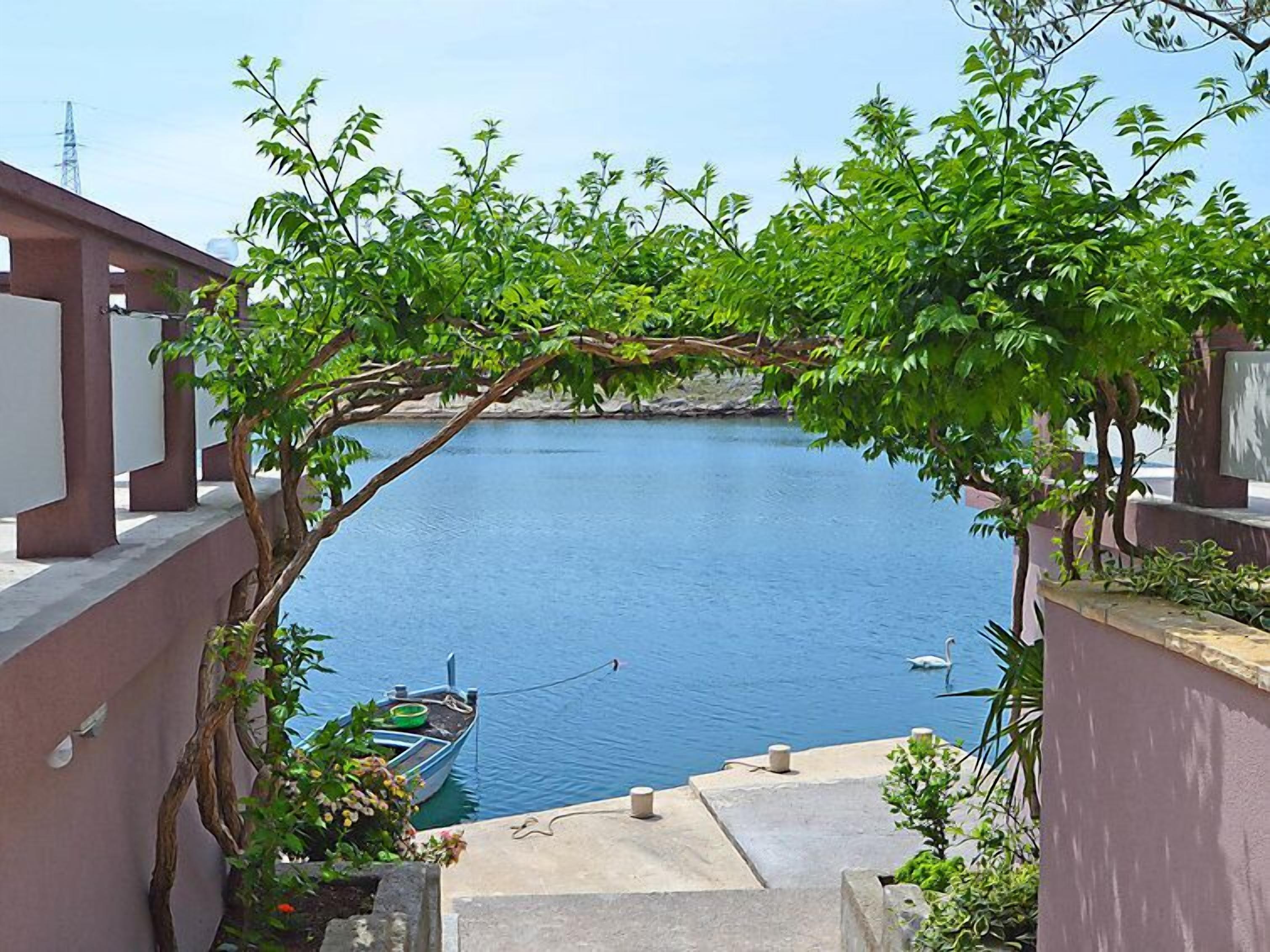 A view of a calm body of water with a boat docked, surrounded by lush greenery and a clear sky.