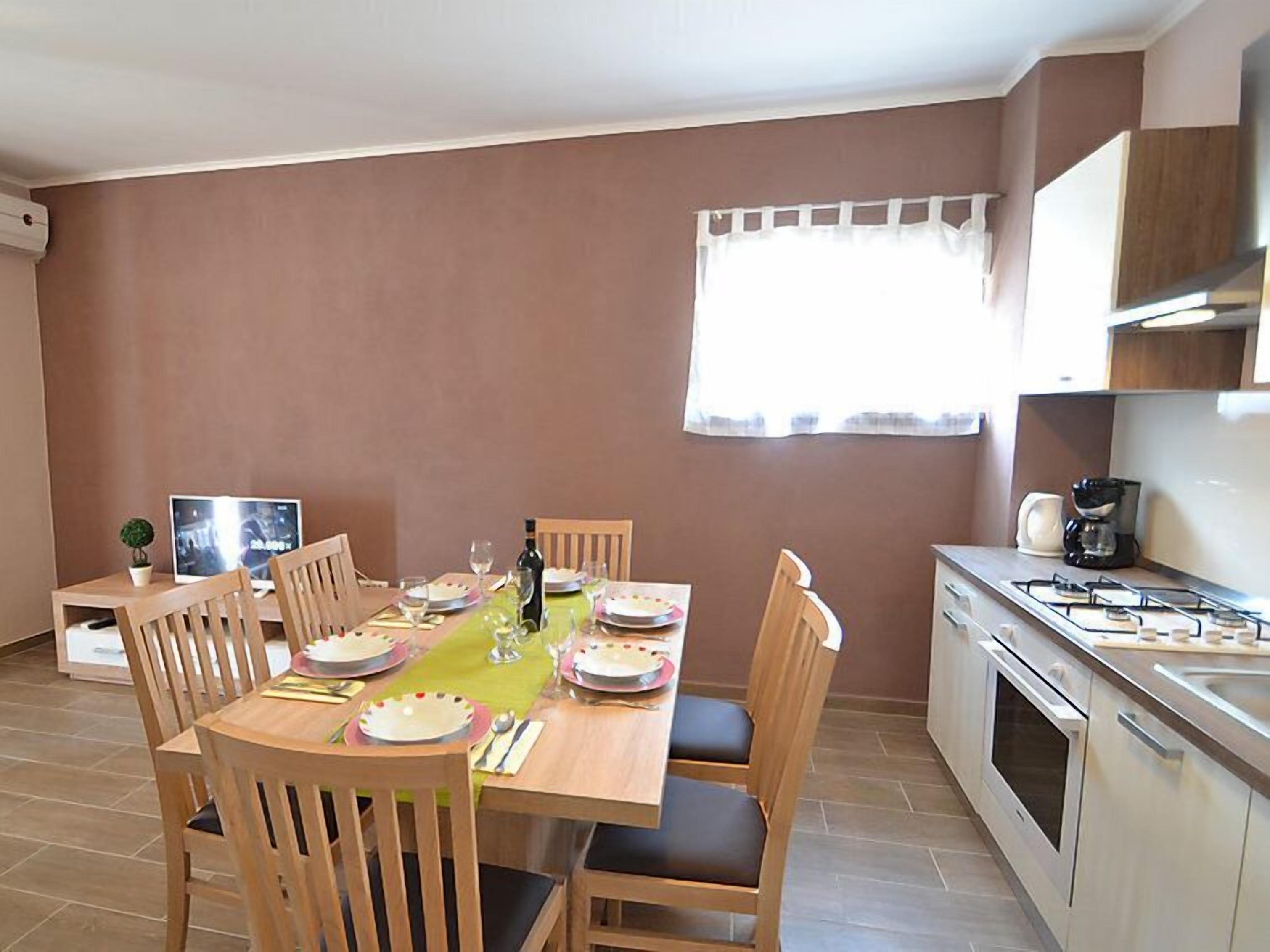 A dining area with a table set for four, wooden chairs, a small potted plant, and a television on a side table.