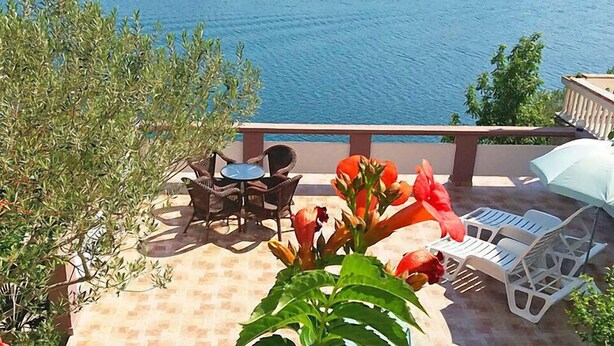 Une terrasse meublée avec des meubles en osier, une table et des chaises, donnant sur une étendue d’eau.