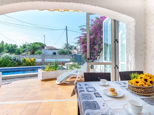 Une terrasse avec une piscine, une table où sont disposés des aliments pour le petit-déjeuner, et une vue sur la verdure et les bâtiments environnants.