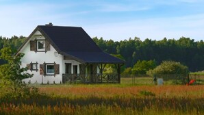 Una casa blanca con techo oscuro, un porche y un campo cercado al frente.
