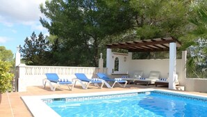 A swimming pool with blue water, surrounded by white walls and a pergola with a roof. There are lounge chairs with blue cushions and a white pillar with a decorative element. - Villa Susan - Private & Peaceful | Pool, Wifi & AC (Sant Antoni de Portmany)