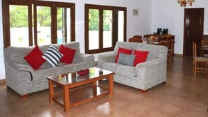A living room with two grey sofas, a wooden coffee table, and a dining area with wooden chairs and a table. - Villa Susan - Private & Peaceful | Pool, Wifi & AC (Sant Antoni de Portmany)
