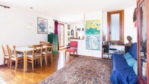 A dining area with a wooden table and chairs, a red chair, and a blue sofa in a bright room with a patterned rug. - On the terraces of Rosa you are constantly forced to look at the sky and Rome (Roma)