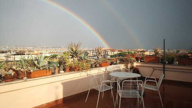 A rooftop terrace with potted plants, a round table, and chairs. - On the terraces of Rosa you are constantly forced to look at the sky and Rome (Roma)