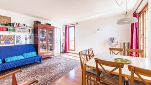 A cozy living room with a blue sofa, wooden dining table, and chairs. There's a bookshelf with books and a cabinet. - On the terraces of Rosa you are constantly forced to look at the sky and Rome (Roma)