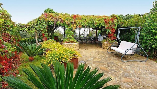 Un pati jardí amb una cadira bressol, plantes en testos i un paviment de pedra.
