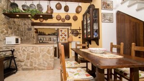 Una cuina rústica amb parets de pedra, bigues de fusta i olles penjades.