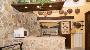 Cuina amb taulell de pedra, microones i planta penjant. Hi ha olles de coure a la paret i una finestra amb vista a l'exterior.