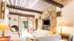 Une pièce chaleureuse avec un mur en pierre, une cheminée, un téléviseur et un coin salon confortable comprenant deux fauteuils et un canapé.