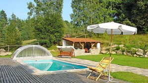 Ein Swimmingpool mit Holzterrasse, einer  überdachten Sitzgelegenheit und einem Steinbau.