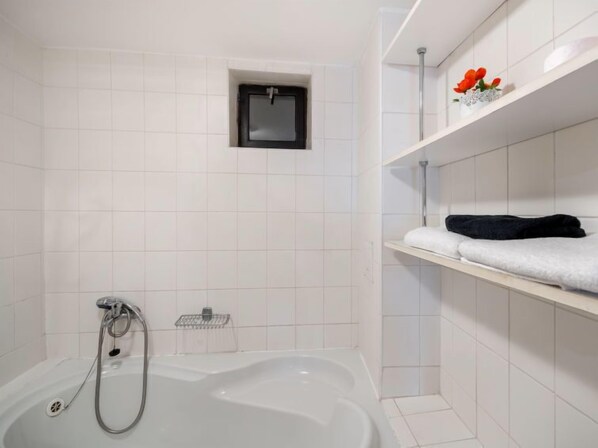 A modern bathroom with a bathtub, a small window, and a shelf with towels and a decorative item.